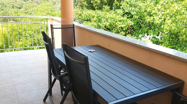 Un balcon avec une table et des chaises, une vue sur la verdure et un sol carrelé.