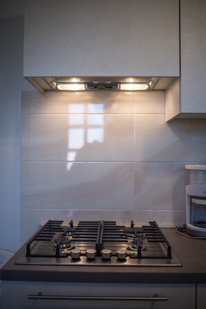 Eine moderne Küche mit Gasherd, Deckenbeleuchtung und einem Fenster, das Licht auf die Spritzschutzwand wirft.