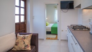 A compact room with a kitchenette, a sofa with a floral pillow, a bed with a green bedspread, and a TV mounted on the wall. - JP2 - studio-apartment for 2 person (Vrbnik)