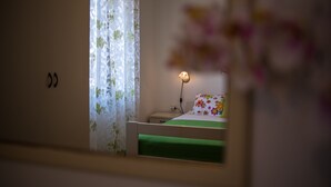 A bedroom with a bed, a nightstand, a lamp, and a floral curtain. - JP2 - studio-apartment for 2 person (Vrbnik)