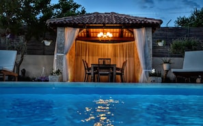 A covered outdoor seating area with a table and chairs, overlooking a swimming pool. - Amazing villa near Split with private pool and playground!!! (Žrnovnica)