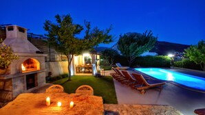 A stone barbecue area with a fire, outdoor seating with lounge chairs, and a swimming pool. - Amazing villa near Split with private pool and playground!!!  (Žrnovnica)