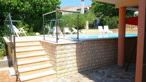Ein Poolbereich mit Stufen zum Pool, umgeben von einer Steinmauer und einem Glasgeländer.