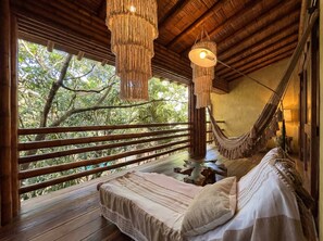 A hammock bed with a view of trees, a wooden ceiling, and a hanging light fixture.