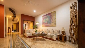 A spacious living area with a sofa, coffee table, and decorative elements like a wall hanging and a wooden sculpture.