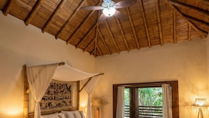 A spacious bedroom with a bed, a ceiling fan, a large window, and a view of greenery outside.