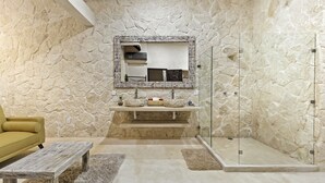 A bathroom with a stone wall, a sink with a mirror above it, a yellow chair, and a wooden bench.