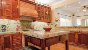 A kitchen with wooden cabinets, a marble countertop, and a central island. - Villa Miramar Aventuras – Luxury Tropical Villa in the Mayan Riviera (Puerto Aventuras)