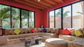 A modern living room with a large sofa set, a coffee table, and a round ottoman. - Villa Miramar Aventuras – Luxury Tropical Villa in the Mayan Riviera (Puerto Aventuras)