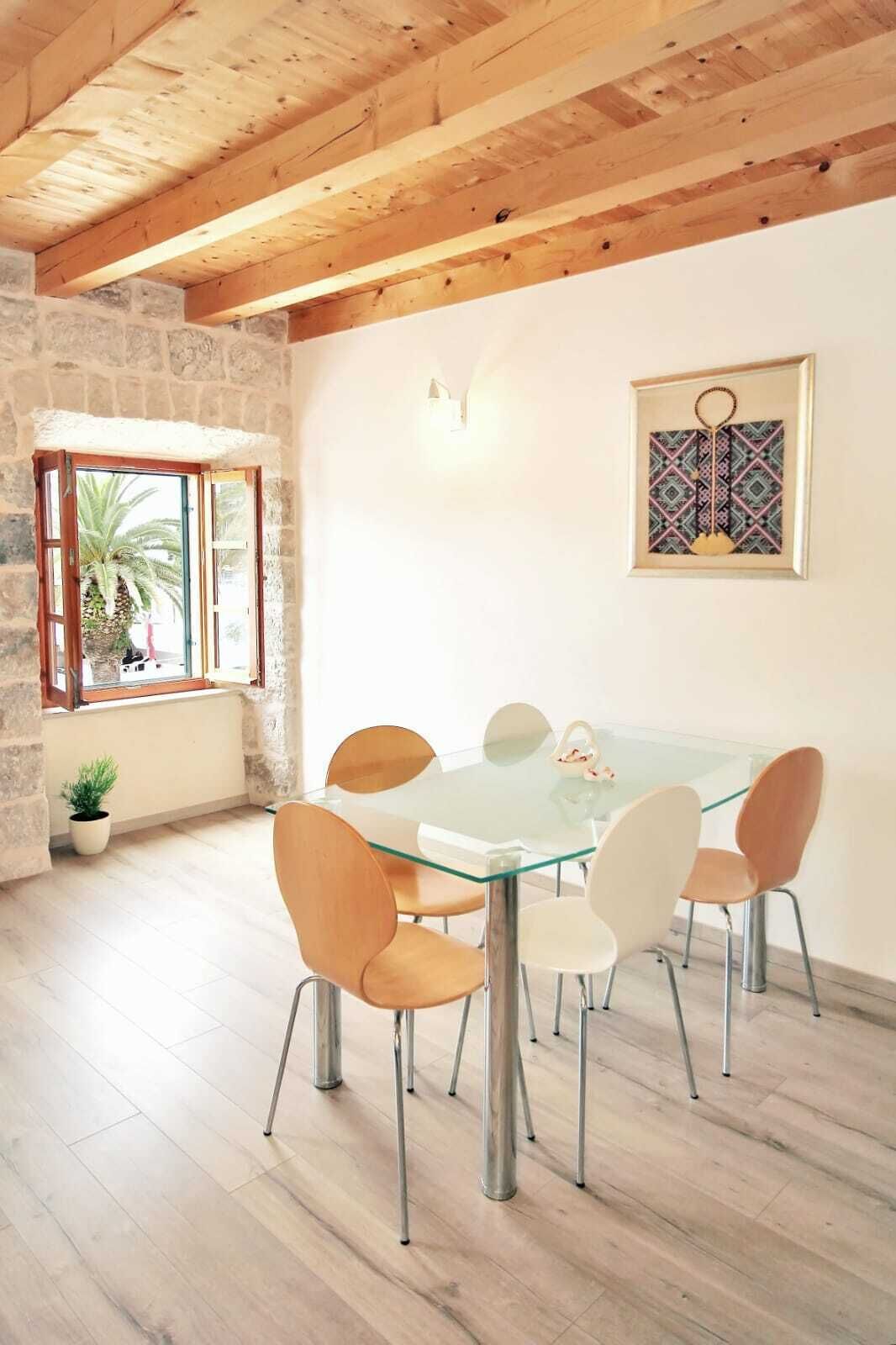 Un espace repas avec une table en verre et des chaises modernes, un mur en pierre et un plafond en bois.