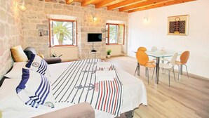 A room with a bed, a TV, a dining table with chairs, and a stone wall.
