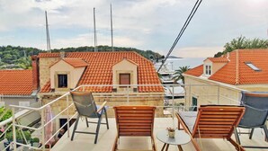 A balcony with outdoor seating, a view of a coastal town, and a building with a tiled roof.