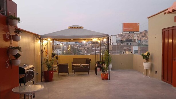Una terraza en la azotea con zona de estar cubierta, una parrilla y plantas en macetas.