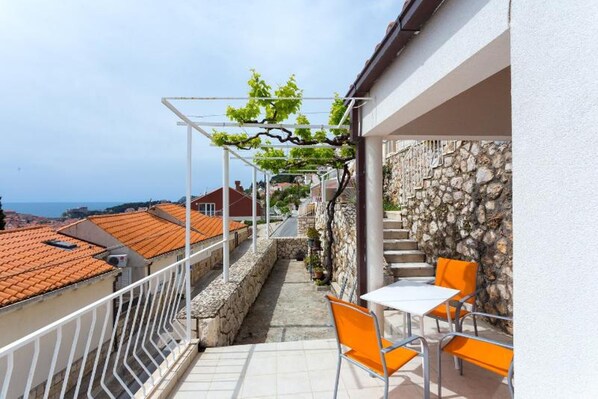 A balcony with orange chairs, a white table, and a stone wall. - Charming Sea View Studio (dubrovnik)