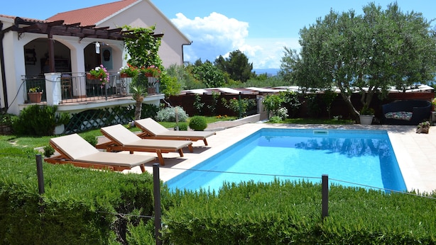 Uma casa com piscina, espreguiçadeiras e um jardim.