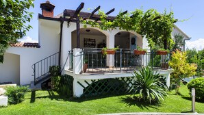 Uma casa de dois andares com varanda, escadas e jardim.