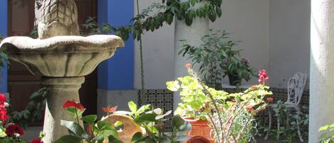 A courtyard with a stone fountain, potted plants, and a white chair.