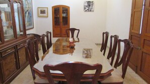 Une salle à manger avec une longue table, des chaises en bois, un buffet et des tableaux encadrés accrochés aux murs.