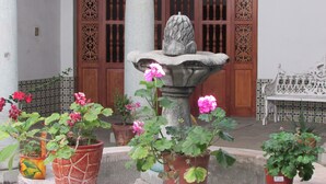 Une cour avec une fontaine en pierre, des plantes en pot et un banc en bois.