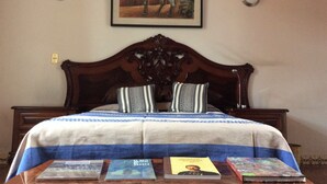 Un lit avec une tête de lit en bois, deux oreillers et une couvre-lit à rayures bleues. Il y a des livres sur une table placée devant le lit.