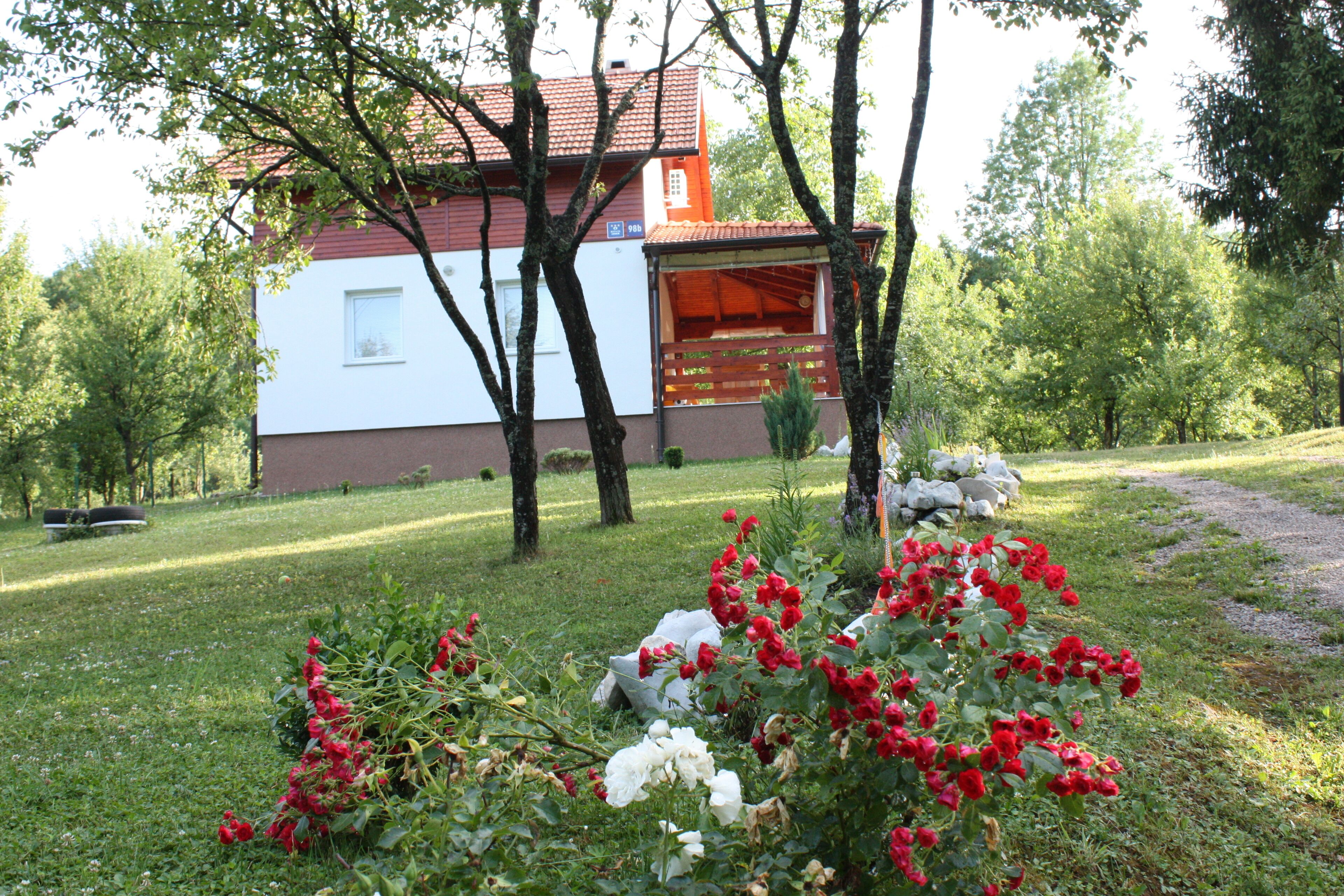 Ein Haus mit rotem Dach und weißen Wänden, umgeben von einem Garten mit roten und weißen Blumen.