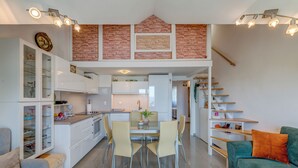 A modern kitchen with a dining area, white cabinetry, a brick accent wall, and a staircase leading to an upper level. - Beautifull attic over the sea and river coust, panoramic sea view (Omiš)