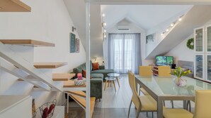 A modern living room with a glass dining table, yellow chairs, a green sofa, and a TV in the background. - Beautifull attic over the sea and river coust, panoramic sea view (Omiš)