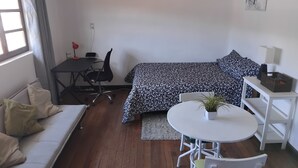 A compact room with a bed, a sofa, a desk with a chair, a small table with a plant, and a white wall with a picture. - Nice apartment in the center of Cusco (Cusco)