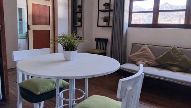 A cozy room with a round white table, two chairs, a sofa with cushions, a bookshelf, and a window with a view of a mountain. - Nice apartment in the center of Cusco (Cusco)