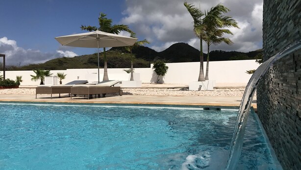 Una piscina con cascada, sillas de descanso y palmeras.