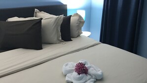 Una cama bien hecha con una toalla y una flor, una pared azul y una ventana con cortinas.