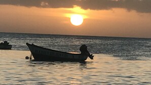 Un bateau nommé « BLESSED GOLDEN FISH » navigue sur des eaux calmes au coucher du soleil.
