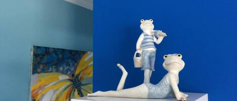 A white shelf with two frog figurines, one standing and one lying down, against a blue wall.