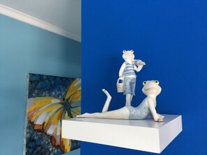 A white shelf with two frog figurines, one standing and one lying down, against a blue wall. - Malika Apartments Blue  Westpunt Curaçao Near Beaches (willemstad)