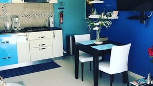 Une cuisine moderne avec des meubles blancs, un mur bleu et un coin repas comprenant une table noire et des chaises blanches.