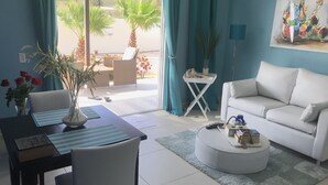 Una sala de estar moderna con un sofá blanco, una mesa de centro redonda y una zona de comedor con un mantel individual a rayas.