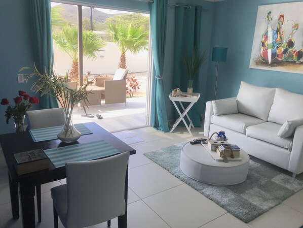 Een moderne woonkamer met een witte bank, een ronde salontafel en een eethoek met een gestreept placemat.
