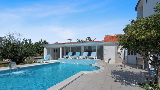 A swimming pool with lounge chairs, a covered seating area, and a patio with a table and chairs.