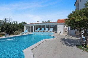 A swimming pool with lounge chairs, a covered seating area, and a patio with a table and chairs. - Villa Almas with swimming pool, summer grill house and tennis court (Neoric)