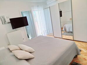 A bedroom with a bed, a flat-screen TV mounted on the wall, a radiator, and a wardrobe with a mirror. - Villa Almas with swimming pool, summer grill house and tennis court (Neoric)