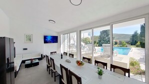 A modern dining area with a large table, chairs, and a TV mounted on the wall.