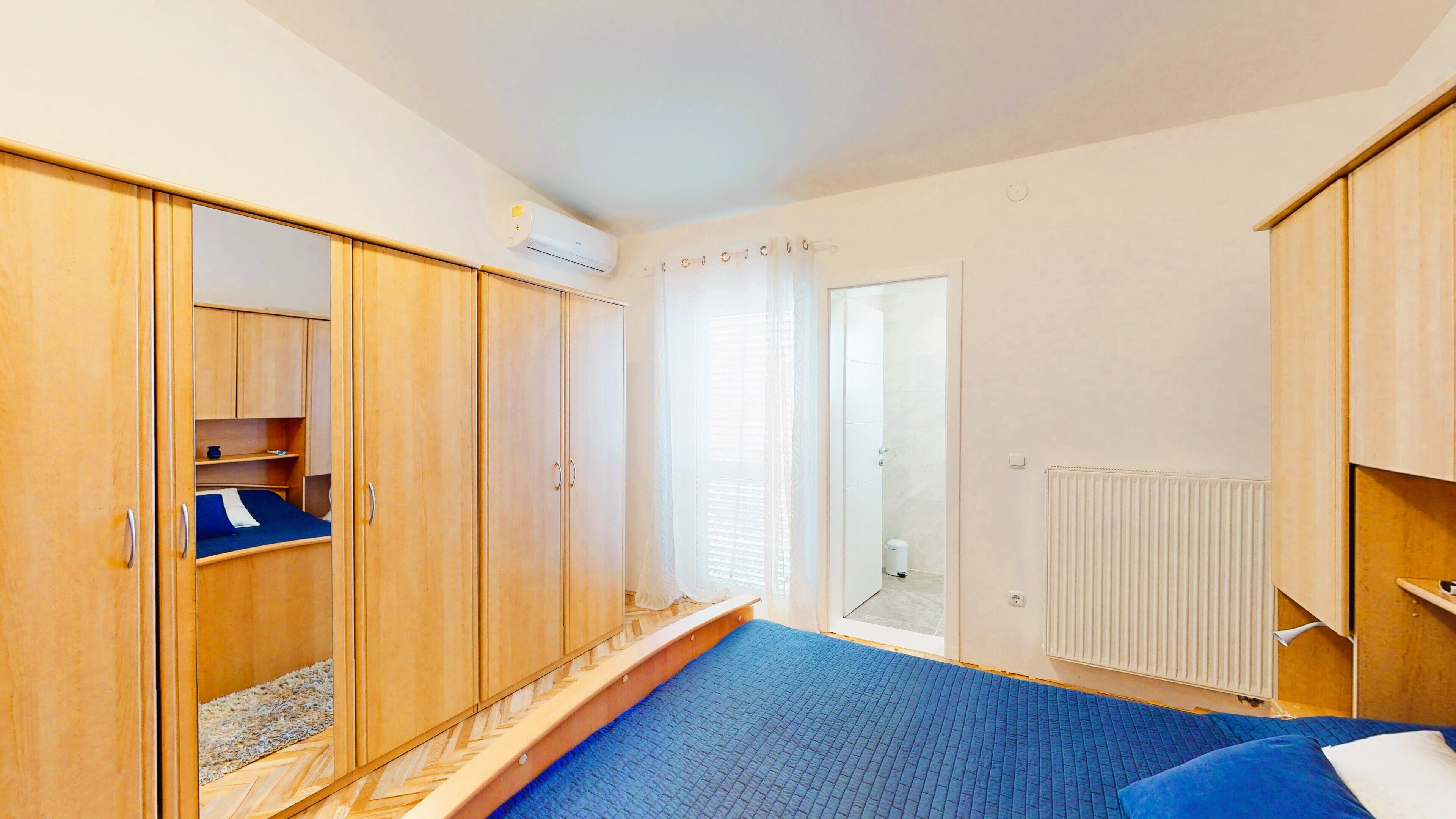 A bedroom with a large wardrobe, a bed with a blue quilt, and a radiator.