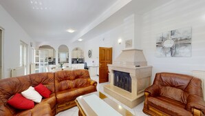 A spacious living room with leather sofas, a fireplace, and a kitchen in the background.