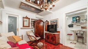Una sala de estar con un sofá, sillones, un televisor, un mueble de madera y una araña.