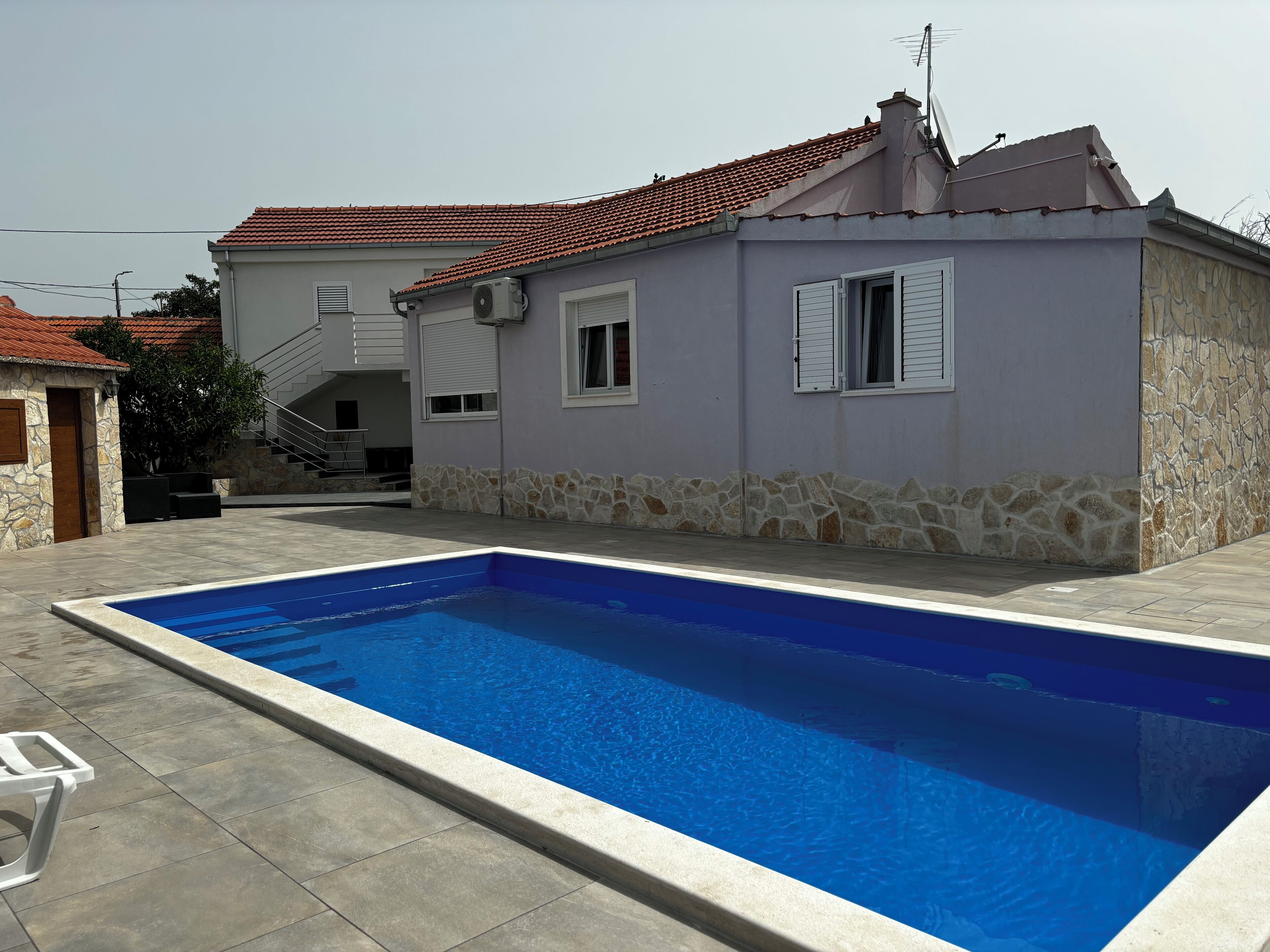 A house with a swimming pool, stone walls, and a red-tiled roof.
