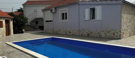 A house with a swimming pool, stone walls, and a red-tiled roof.