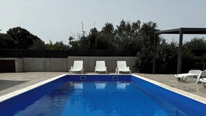A rectangular swimming pool with clear blue water, surrounded by a tiled deck. There are four white lounge chairs aligned along the pool's edge. The pool area is enclosed by a low wall with a dark-colored gate on the left. - Hidden Villa **** With Private Pool In Peaceful Area  (Vinišce)