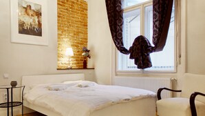 A bedroom with a brick wall, a bed with white linens, a chair, a table, and a window with curtains. - Deluxe apartment with super Wifi in city center (Budapest)