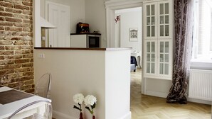 A kitchen with a microwave, a coffee maker, and a brick wall. There is a dining area with a table and chairs, and a window with curtains. - Deluxe apartment with super Wifi in city center (Budapest)