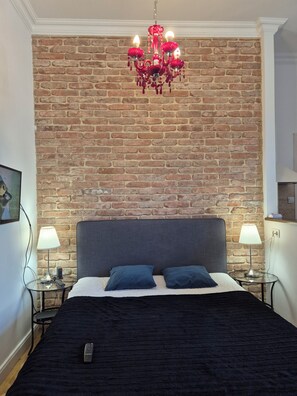 A bedroom with a brick wall, a chandelier, a bed with two pillows, and bedside lamps.
